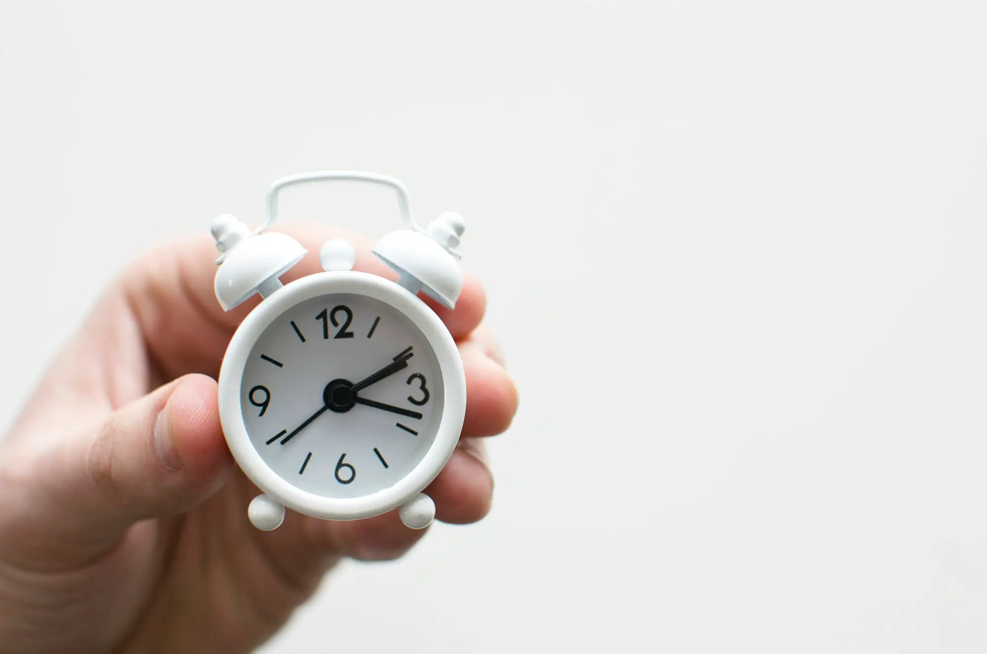 Hand holding a small bell alarm clock